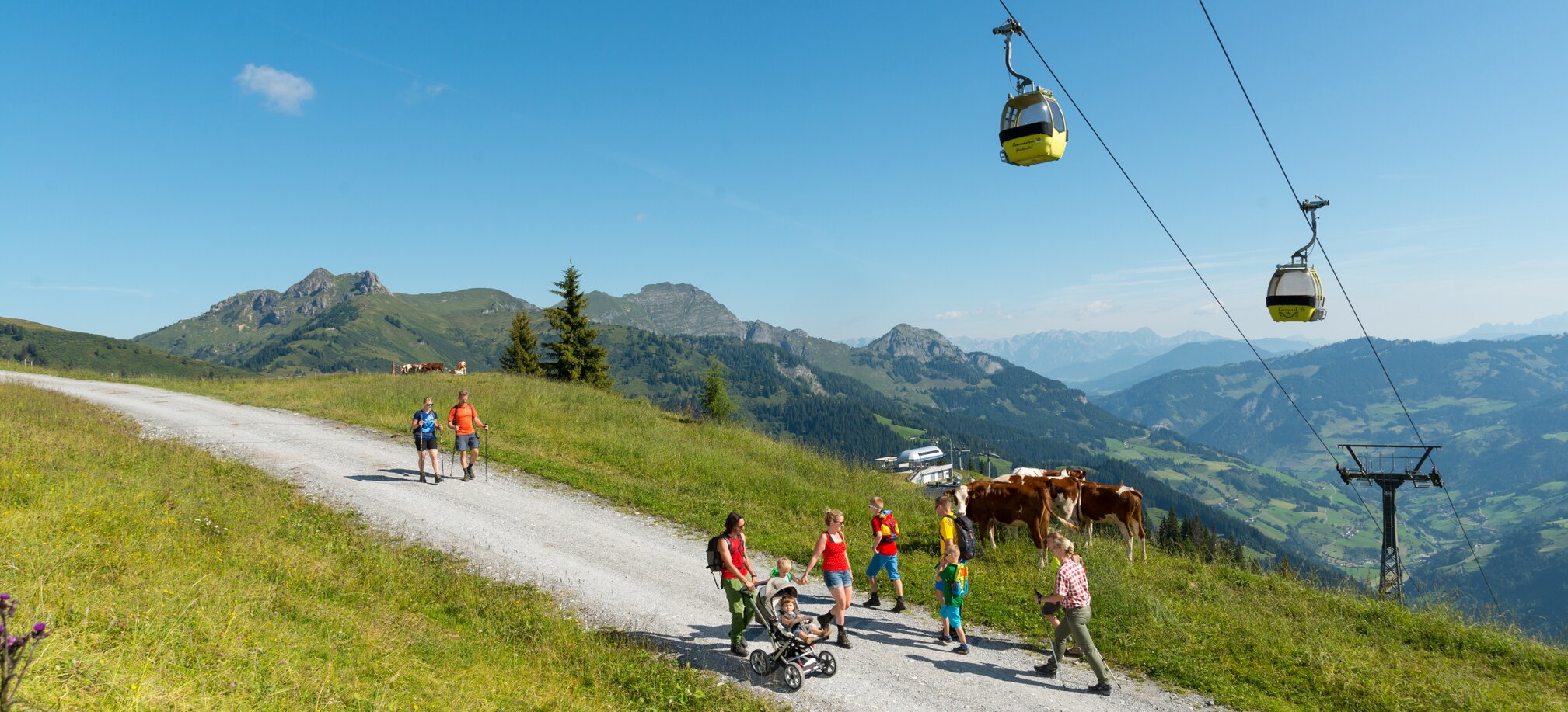 People walk up the mountain on a gravel road under a cable car