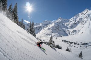 Skier freeriding in open terrain with sunlit snow-covered mountains in the background | © Gasteinertal Tourismus GmbH | Christoph Oberschneider
