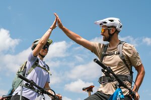 Zwei Mountainbiker geben sich auf ihren Rädern ein High Five unter blauem Himmel mit einzelnen Wolken | © Hochkönig Bergbahnen