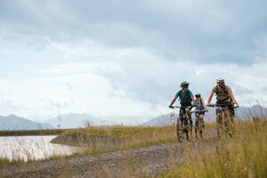 Drei Mountainbiker fahren auf einem Schotterweg am Speicherteich bei der Bürglalmbahn in Dienten | © Hochkönig Bergbahnen