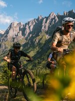 Drei Mountainbiker fahren in Mühlbach auf einem Weg vor steilem Felsmassiv nahe der Karbachalmbahn. | © Hochkönig Bergbahnen