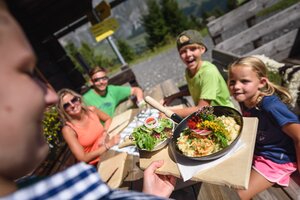 Eine Servicekraft bringt einer Familie auf der Sonnenterrasse der Karbachalm in Mühlbach ein Gericht mit Salat. | © Hochkönig Bergbahnen