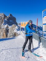 Skifahrerin prüft ihr LVS-Gerät an einem Safety-Checkpoint vor beeindruckender Felskulisse. | © René Eduard Perhab