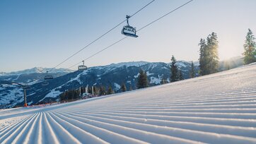Perfekt präparierte Skipiste am frühen Morgen mit Sessellift und Bergen im Hintergrund | © Snow Space Salzburg