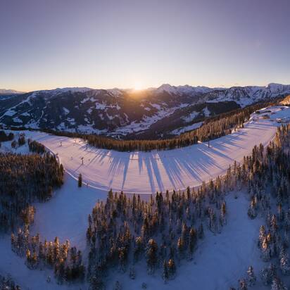 Blick auf verschneite Pisten am Grafenberg mit Sonnenaufgang, verschneiten Bäumen und Bergpanorama | © Snow Space Salzburg