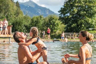 Family enjoying joyful swim in natural lake with mountains and bathers in background | © TVB Eben, Lorenz Masser