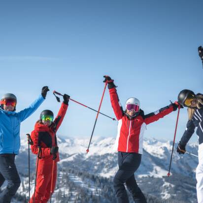 Vier Freunde in Skiausrüstung stehen auf der Piste und Strecken die Arme freudvoll in die Höhe. | © Ski amadé
