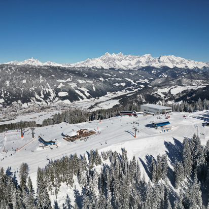 A gondola station, two chairlift stations and a ski hut from above and many houses can be seen in the valley below
