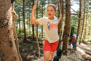 Mädchen balanciert auf Reifen im Waldseilgarten, weitere Kinder klettern im Hintergrund. | © Shuttleberg