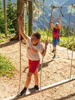 Mädchen balanciert auf Holzsteg im Seilgarten, Frau klettert im Hintergrund. | © Shuttleberg