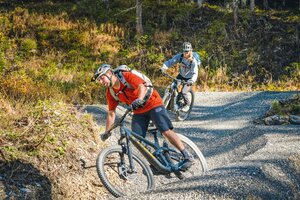 Zwei Mountainbiker fahren in Schräglage durch eine enge Kurve auf dem Schottertrail. | © Shuttleberg