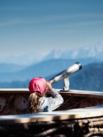 Mädchen mit roter Kappe blickt durch ein Fernrohr auf Bergpanorama von einer Aussichtsplattform in Zauchensee. | © Matthias Fritzenwallner