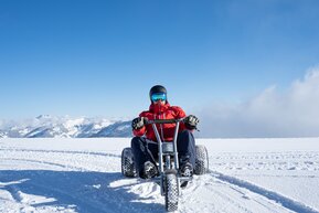 Person riding a mountaincart across snowy high plateau with alpine view and blue sky in Dorfgastein | © Dorfgasteiner Bergbahnen