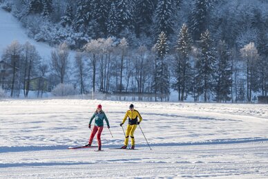 Two cross-country skiers on groomed trail in winter landscape with snowy trees in the background | © Salzburger_Sportwelt_Lorenz_Masser