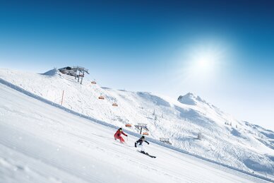 Two skiers carving down a freshly groomed slope on a sunny day | © Ski amadé
