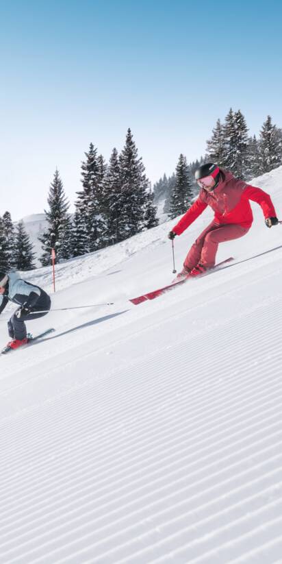 Two skiers ski in parallel on freshly groomed slope with powder snow and sunlight in Ski amadé