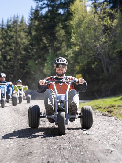 Gruppe fährt mit Mountaincarts rasant bergab auf Schotterweg durch Waldgebie | © Dorfgasteiner Bergbahnen AG