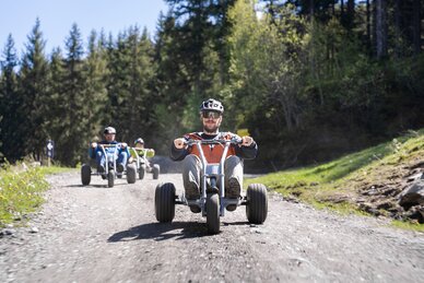 Group rides mountain carts downhill on gravel path through forested alpine terrain | © Dorfgasteiner Bergbahnen AG