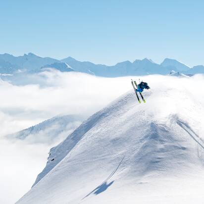 Skier doing a backflip over a snow dome and all around are snowy mountains and a blue sky | © Gasteinertal Tourismus GmbH, www.oberschneider