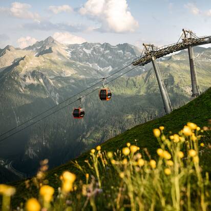 Two red gondolas of the gastein lift over blooming meadow and green valley in Gastein | © Gasteiner Bergbahnen AG, Marktl Photography