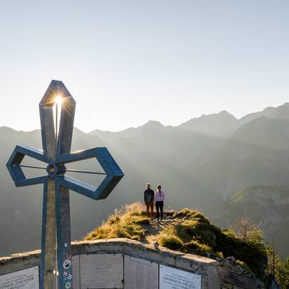 Two women at Graukogel summit cross, sunrise behind mountains, overlooking stunning alpine panorama | © Skigastein, seven frames
