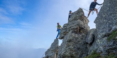 Drei Kletterer sichern sich am schroffen Felsgrat der Schlossalm in Gastein unter blauem Himmel | © Balazs Kovacs