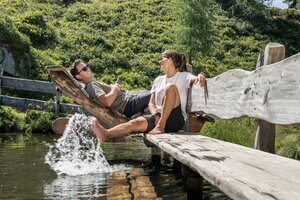 Couple relaxing on wooden loungers with feet in mountain water at Graukogel | © Skigastein, seven frames