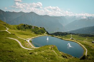 Speichersee auf der Schlossalm mit Wasserfontänen, umgeben von Wanderwegen und Almlandschaft in Gastein | © Gasteiner Bergbahnen AG