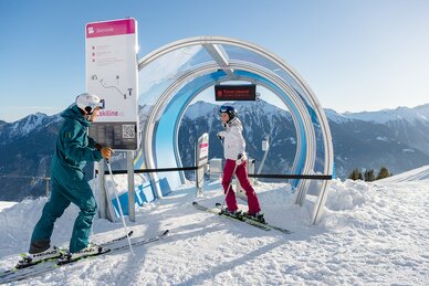 A couple on skis stands in front of the start of a skimovie track and talks | © Gasteiner Bergbahnen AG, Wolkersdorfer