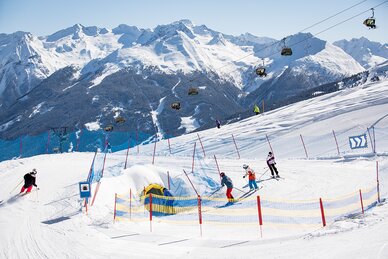 Four people ski on a funslope towards a tunnel and in the background you can see a slope | © Roland Haschka