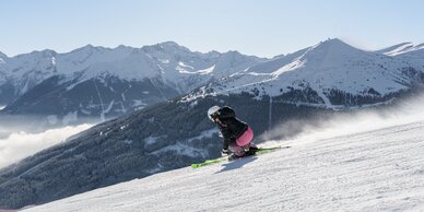 Skier carving on a slope with view of snowy forests and high mountains | © Simon Hutter
