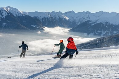 Three skiers including two kids skiing downhill with sunny alpine mountain view | © Simon Hutter