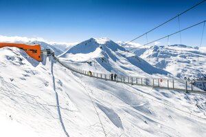 Suspension bridge spans a snow-covered precipice and at one end is an orange mountain station of a cable car | © Gasteiner Bergbahnen AG, Wolkersdorfer