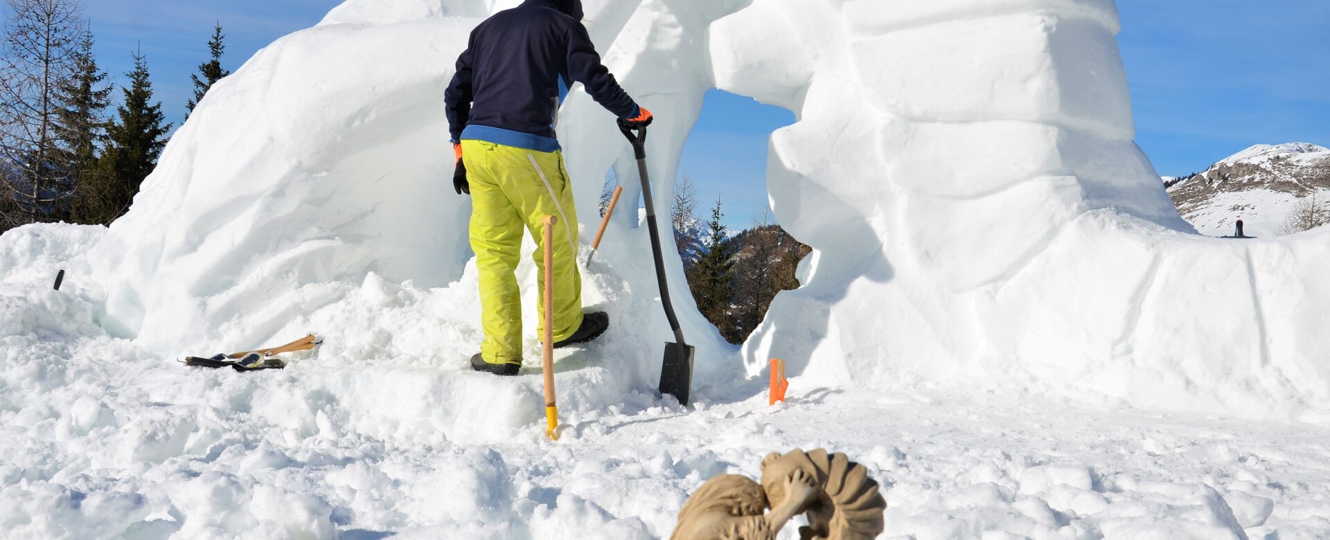 Person arbeitet an großer Schneeskulptur, Tonmodell des Drachen im Vordergrund sichtbar