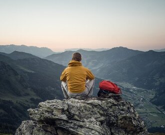 Ein Mann sitzt auf einem Felsen und betrachtet den Sonnenuntergang über den Bergen | © Gasteinertal Tourismus GmbH - moodley