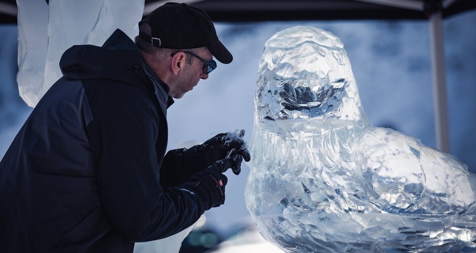 An artist in gloves carves a detailed ice sculpture shaped like a bird at the Art on Snow Festival. | © TVB Dorfgastein, Max Steinbauer