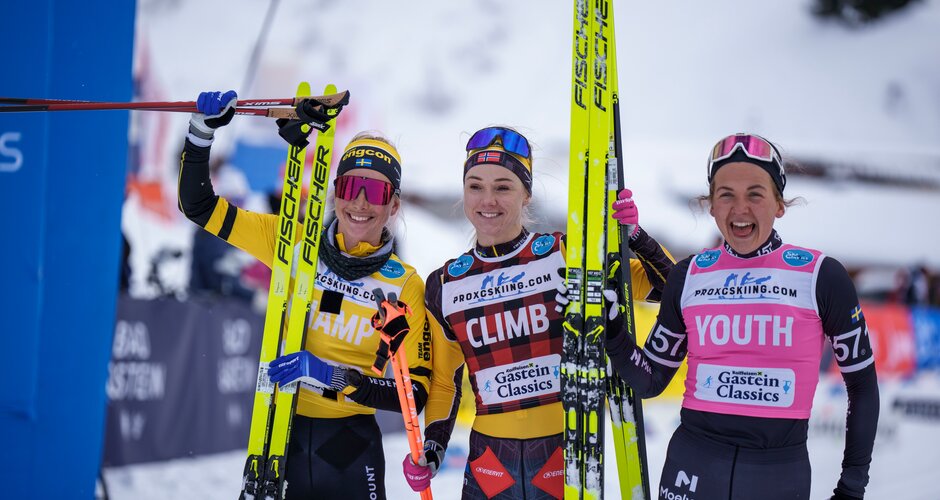 Three female skiers in race suits hold skis and smile at the camera after finishing the competition. | © Gasteinertal Tourismus, Christoph Oberschneider