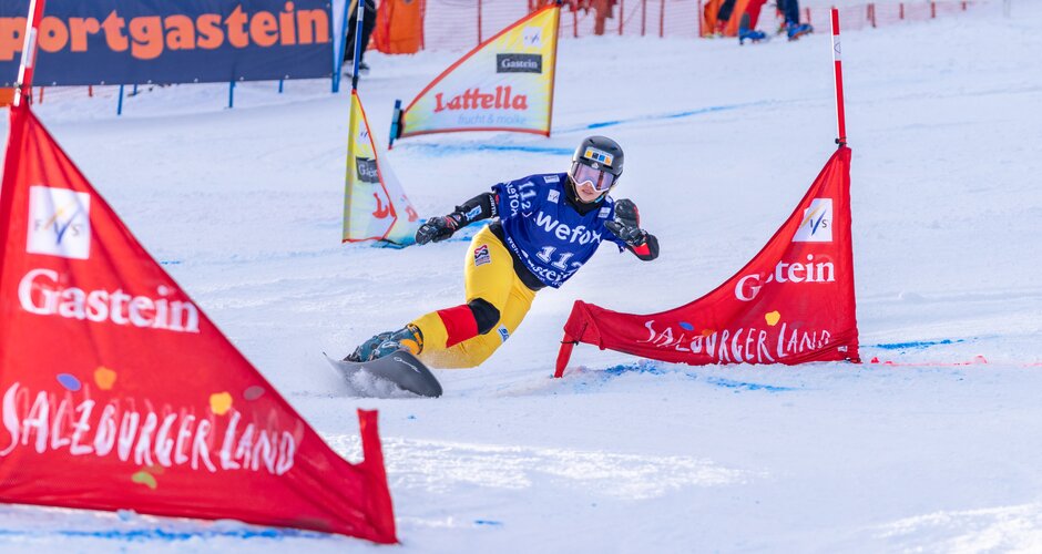Snowboarder in yellow pants carves hard around a red gate during World Cup race in snowy Gastein. | © KTVB Bad Gastein, Simon Hutter