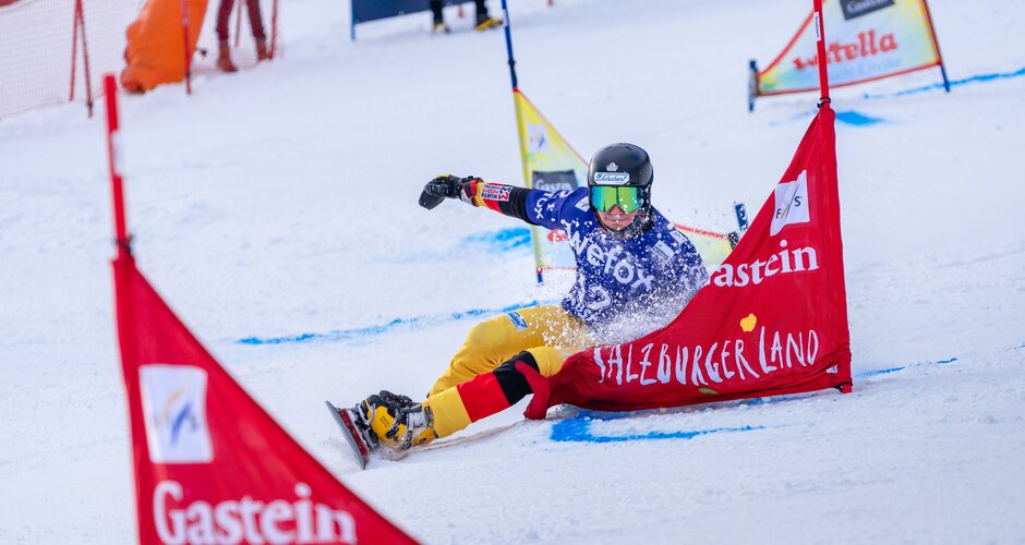 Snowboarder in yellow pants carves sharply around red gate during World Cup race in snowy Gastein. | © KTVB Bad Gastein, Simon Hutter