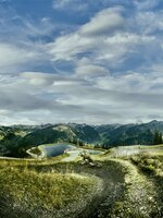 Mountain biker on winding trail overlooking reservoir, forested slopes and a sky full of dramatic clouds. | © Großarler Bergbahnen