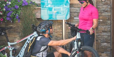 Zwei Radfahrer laden ihre E-Bikes an einer Ladestation am Hochkönig in sommerlicher Bergkulisse