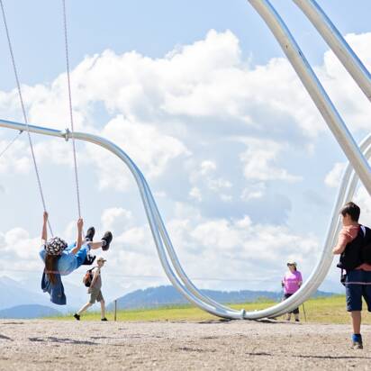 Kinder schaukeln auf überdimensionalen Schaukeln im Schaukelpark Hochkönig vor Alpenkulisse bei Sonnenschein | © Manu Lochner