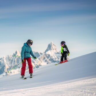 A child with rides with his dad in front of a mountain peak on freshly groomed piste. | © Snow Space Salzburg