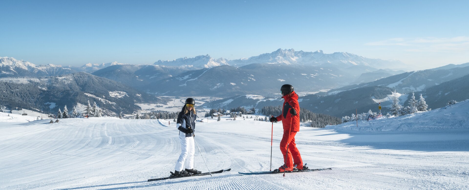 Two skiers stand on a freshly prepared piste, one looks down into the valley and the other looks up | © Ski amadé