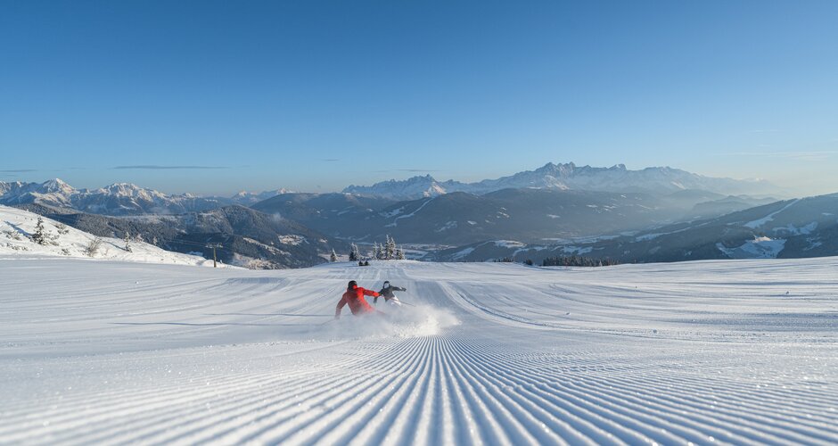 Two people ski down a freshly groomed slope and swirl up the snow | © Ski amadé