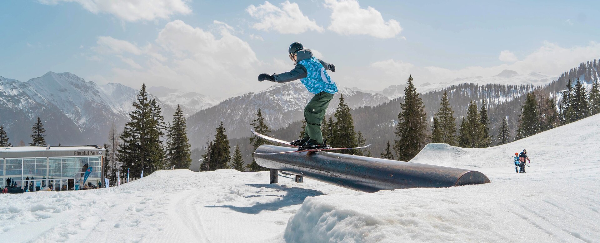 Skier balancing on rail in sunny snow park with snowy alpine mountains in background | © Shuttleberg / Absolut Park
