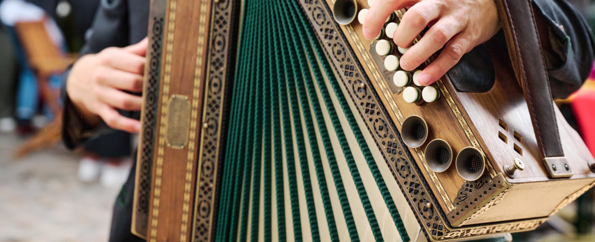 Someone is playing an accordion which has the colours light brown and green. | © Matthias Fritzenwallner