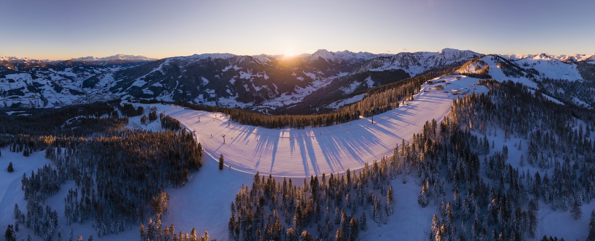 Panorama picture of a ski mountain and behind the surrounding snow-covered mountains the sun is just rising | © Snow Space Salzburg