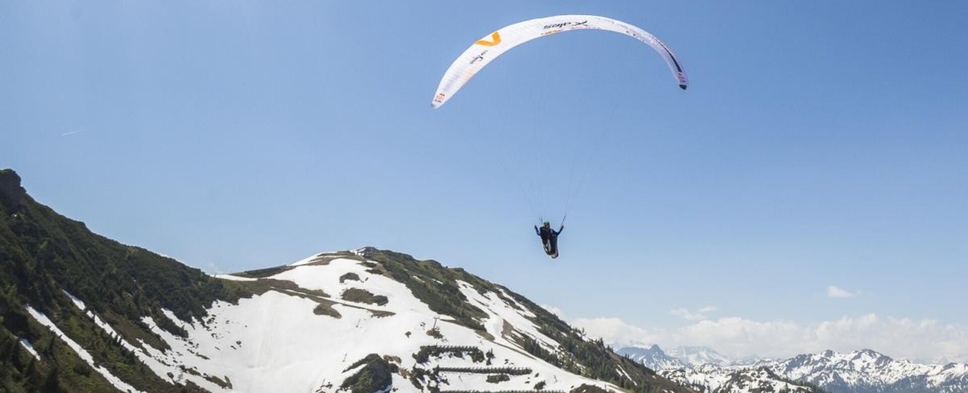 Zwei Paragleiter fliegen über schneebedeckte Alpen bei blauem Himmel mit Wolken.