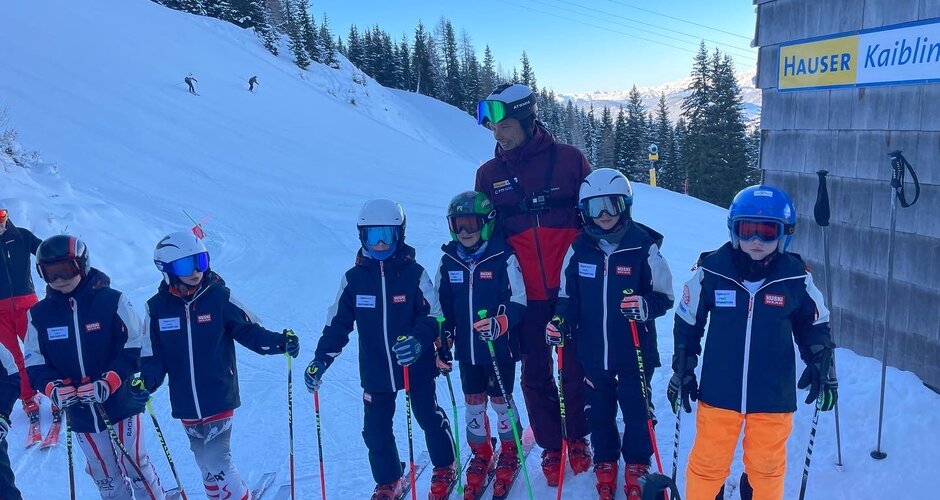 Sechs Kinder stehen nebeneinander neben dem Starthaus der Skirennstrecke und hinter ihnen steht Thomas Sykora | © Hauser Kaibling
